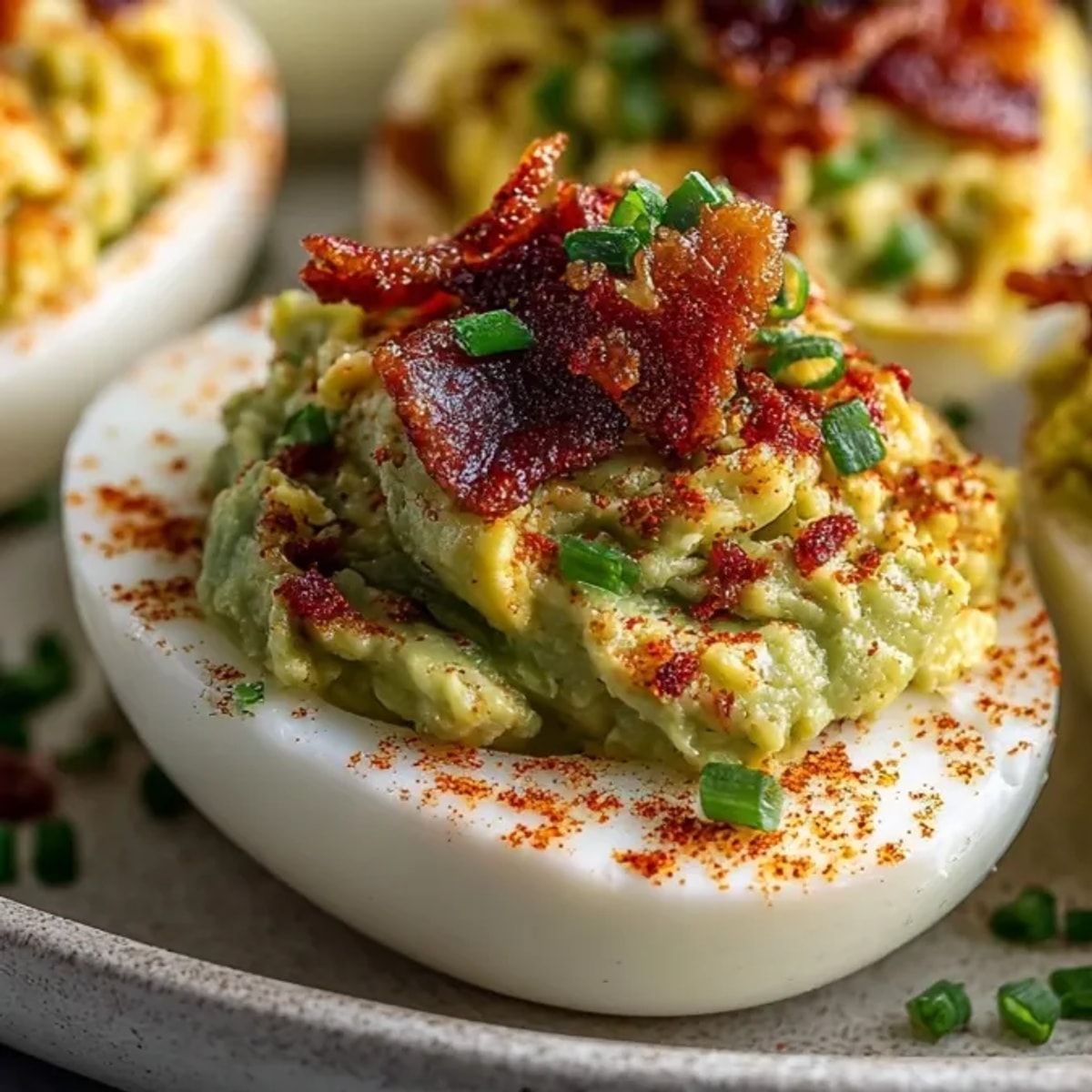 Creamy and savory Deviled Eggs with Avocado & Bacon, topped with smoky paprika.