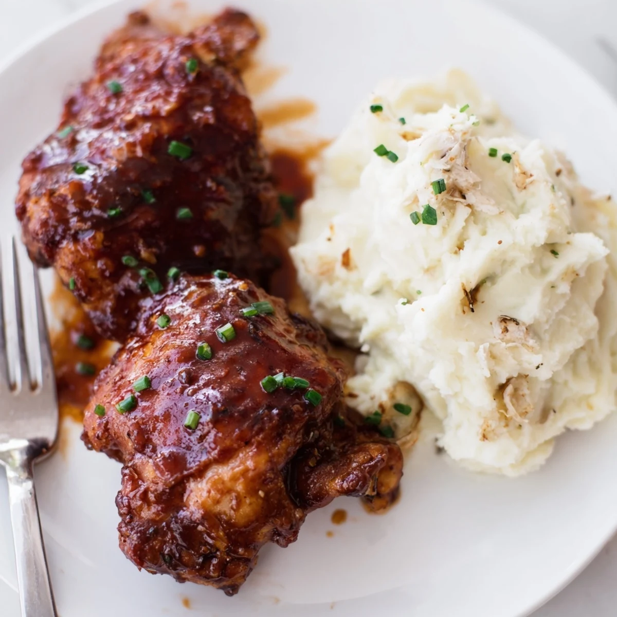 Oven-baked honey BBQ chicken thighs paired with creamy garlic mashed potatoes on a plate.  