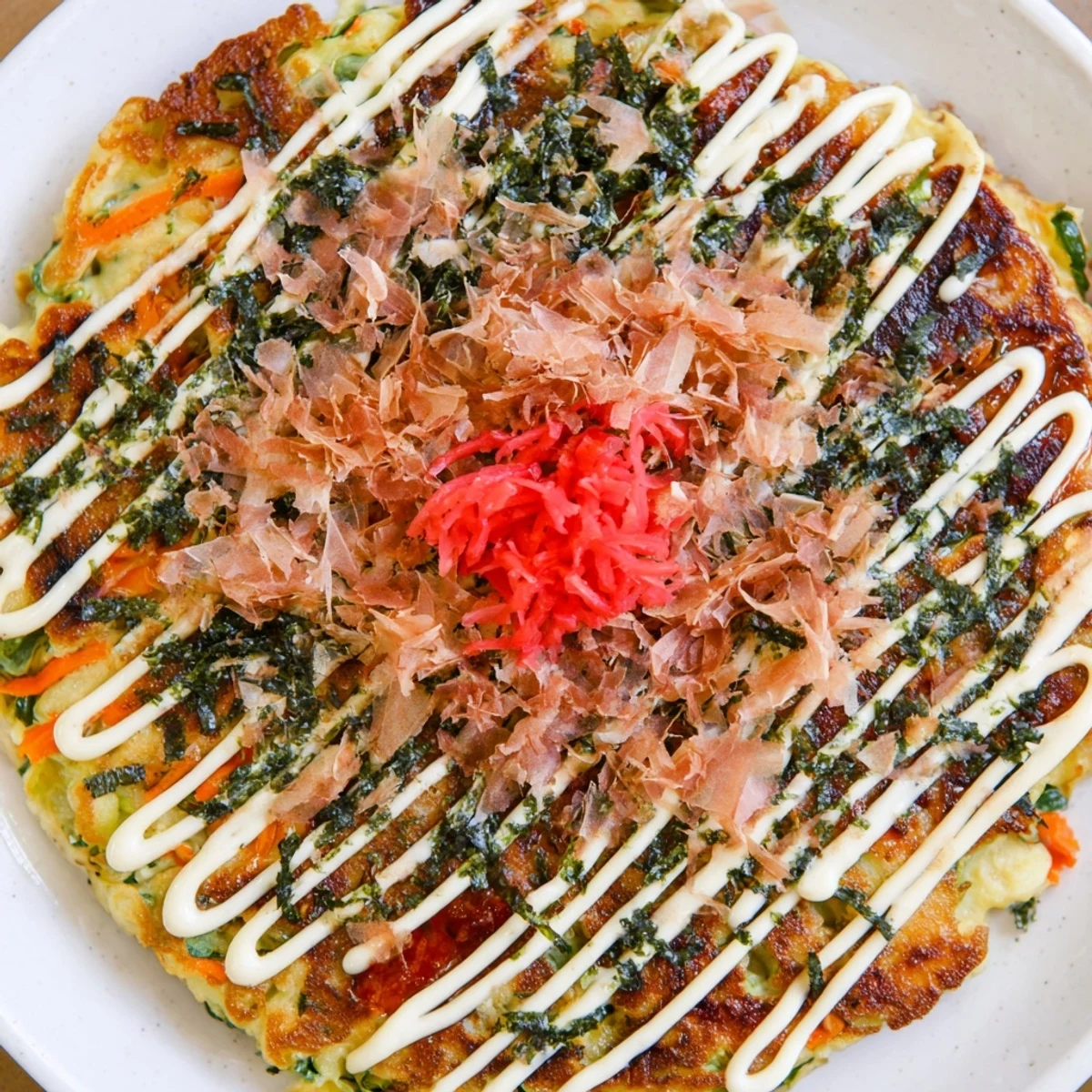This plate of flavorful Okonomiyaki pancakes is topped with scallions and savory okonomiyaki sauce.
