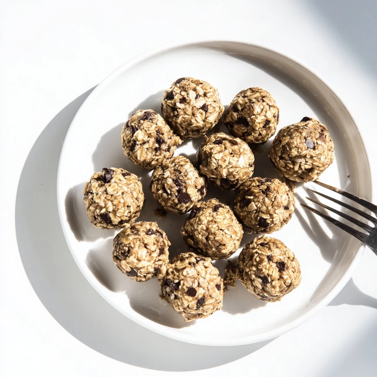 Freshly rolled Banana Chocolate Chip Energy Balls sit on a white plate, with mashed banana and oat ingredients nearby for context.