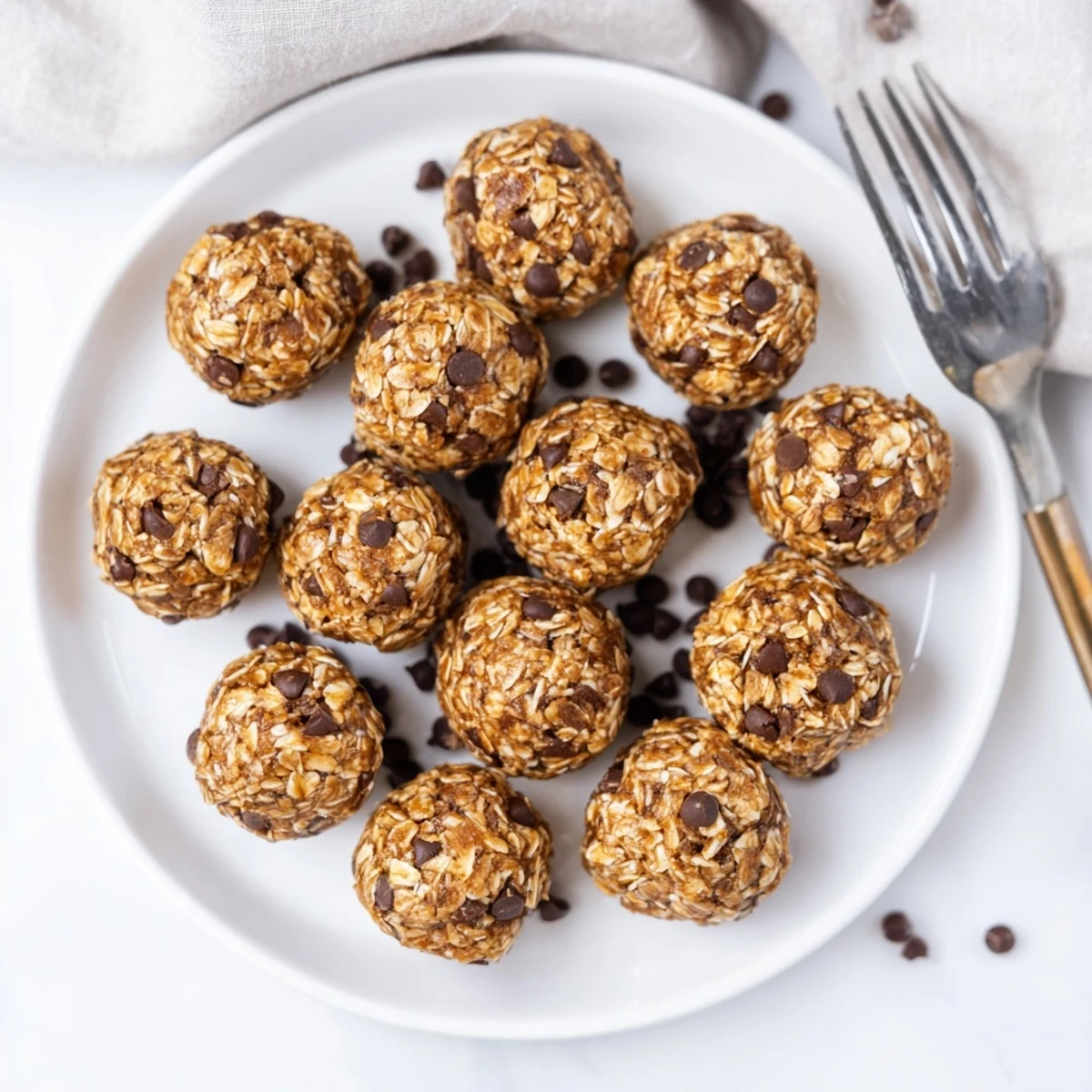 A hand holding a bite-sized Banana Chocolate Chip Energy ball reveals its soft, crumbly interior studded with chocolate chips.