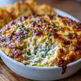 A baked bowl of warm Crack Corn Dip with golden cheesy top, served with tortilla chips for dipping.