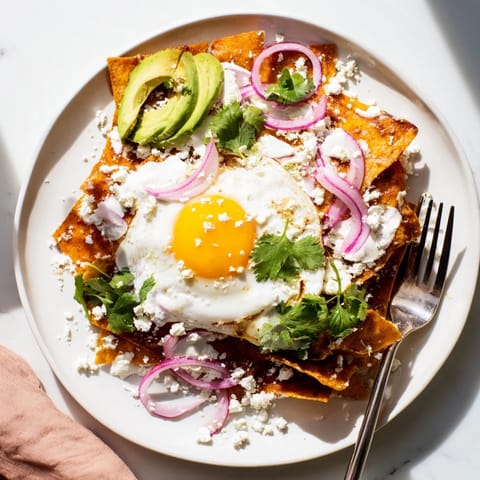 Golden-fried tortilla triangles tossed in spicy red salsa, garnished with cilantro, red onion, and a dollop of sour cream on this hearty plate of Chilaquiles.