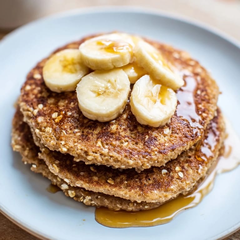 Freshly cooked banana oat pancakes, drizzled with sweet maple syrup and topped with berries.