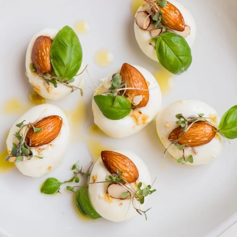 Fresh The Polished Pebble appetizer, showcasing creamy, oval cheeses and golden roasted almonds, drizzled with oil.