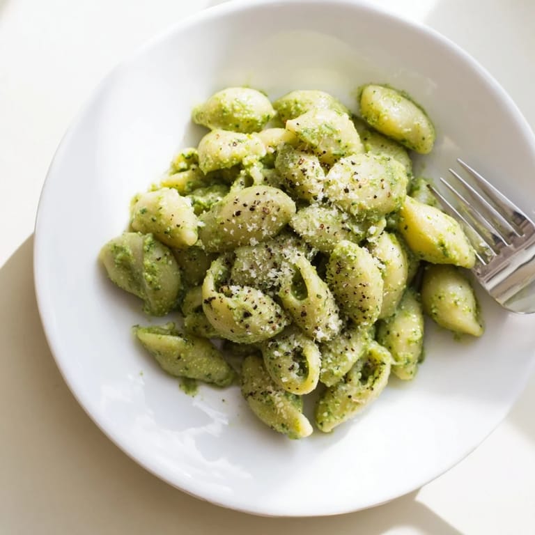 A close-up of Creamy Avocado Pesto Mac, highlighting the silky avocado pesto clinging to each piece of pasta, garnished with a lemon wedge.