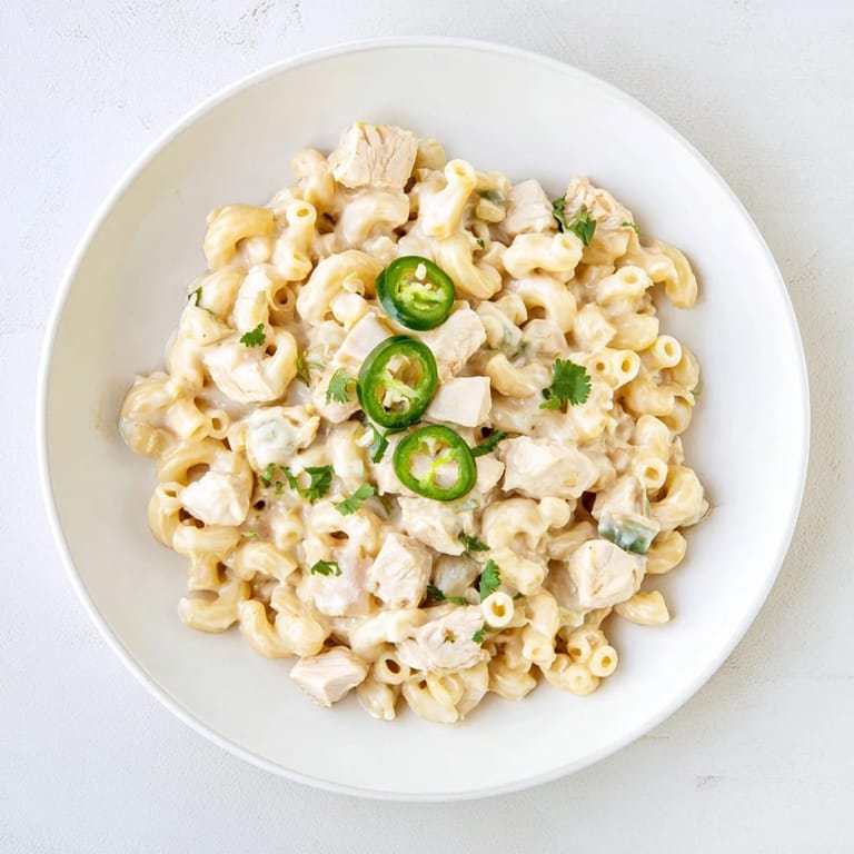 A spoon lifts a cheesy serving of Green Chili Chicken Mac, showcasing tender chicken pieces and mild diced green chiles throughout.