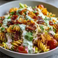 Vibrant taco pasta salad with Doritos, avocado ranch dressing, and fresh vegetables in a colorful bowl.